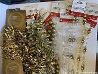 Photo showing the full set of 11 new decorative garlands with tags, featuring shiny gold and silver tinsel, gold ball, clear crystal, silver and gold beaded plastic garlands.