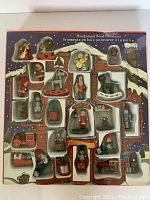 Set of 24 hand painted wooden Christmas ornaments displayed in packaging, showcasing various figurines such as Santa, animals, nutcracker, train, and holiday objects.