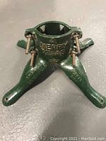 Green cast iron Christmas tree stand with four legs and two interlocking pieces, showing embossed text and screws.