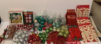 Wide shot showing assortment of boxed and loose plastic and satin-covered Christmas ornaments, decorative bows, and ribbon rolls.