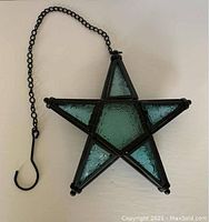 Front view of the hanging blue glass star showing the black metal framing and embossed blue glass panels connected with metal hinges and the metal chain attached for hanging.