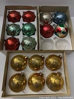 Photo displaying 16 large vintage glass Christmas balls in three boxes arranged by color and type, showing red, green, turquoise, gold, silver, blue, and multicolor pieces, some with glitter swirl designs and some gold ribbed texture.