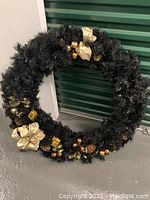 Full frontal view of the black oversized wreath measuring 34 inches across with gold decorations including bows, pine cones, ornaments, and gift boxes.