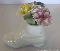 Side view of the white ceramic boot holding yellow, pink, and blue flower bouquet figurine on plain surface.