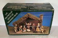 Original boxed set showing the nativity scene figurines arranged in front of the wooden creche roofed with moss. Box has visible wear and damage.