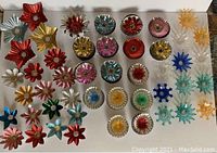 Top-down view showing the full spread of over 80 assorted vintage Christmas tree light reflectors, arranged by shape and color, highlighting the variety in design and material.