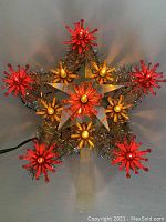 Front view of the vintage lit star-shaped Christmas tree topper showing gold metal frame, translucent central star, and red and gold bulb starbursts with tinsel.