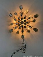 Lit vintage star tree topper with heavy metal construction and clear crystals photographed hanging against a white background, showing the brightness of the small lights and crystal brilliance.