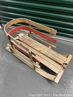 Angle view showing the wooden sled with red trim and metal handles, highlighting overall condition and wear.