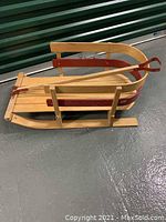 Side view of wooden sled showing wood slats, red metal side trim and pull handle with loop