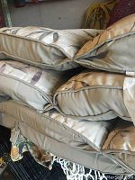 Stack of 5 beige outdoor chair cushions with floral leaf pattern and ties, showing side and top views of the cushions piled together.