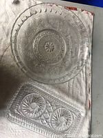 Two clear glass dishes on white towel background, one large round patterned dish and one smaller rectangular pinwheel patterned dish.