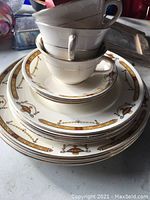 Image of stacked antique Surrey Bridgwood China teacups and plates showing the gold and brown decorative patterns on white china.