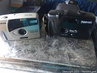 Photo showing the Fujifilm Clear Shot 60 AF Date camera and Wide Pic Panorama camera side by side on a metallic surface.