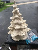 Full view of the white ceramic Christmas tree placed on a black cushioned surface outdoors.
