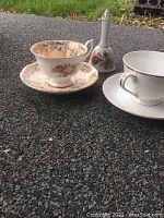 Two china cups with matching saucers displayed on the ground, showing the floral rose patterned set and the decorative bell at the back.