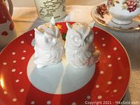 Photo of two white ceramic owl-shaped salt and pepper shakers placed on a Christmas-themed red plate with white polka dots and a polar bear design.