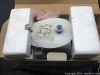 Overhead photo of Dressmaker II sewing machine packed in box with two white styrofoam blocks on each side, blue bobbin on the top spool pin.