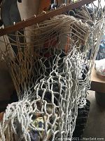 Close-up view of the white rope netting and wooden spreader bar with hooks attached to the hammock.