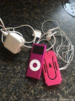 Apple iPod Nano 4th Gen pink with charging adapter, earphones, and protective case on a dark countertop.