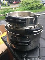 Stacked view of two stainless steel pots and one colander showing side handles and pot rims.