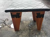 Front view showing wooden legs with black train silhouettes and black cushioned seat with diamond pattern.