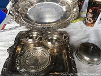 Silver pieces displayed on a white cloth including two trays, cream and sugar set, lidded dish, and glass insert.