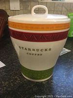 Front view of Starbucks Coffee ceramic cookie jar showing colorful bands and text on a dark counter surface.