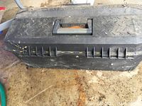 Top view of the black plastic tool box showing the carrying handle and textured surface with yellow paint marks.