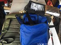 Photo showing four brand bags stacked: olive green Under Armour padded bag, black Thermos cooler bag opened to show silver insulated interior, blue Nike bag with logo visible, blue backpack with black zippers.
