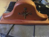 Photo showing full view of wooden mantle clock with curved top and black starburst with metal number markers