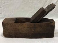 Side view of the antique wooden hand plane showing the angled blade and wooden wedge.