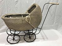 Side view of the original primitive wicker child baby carriage showing wicker body, curved hood, and metal frame with handle and wheels.