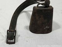 Side view of vintage metal cowbell attached to leather strap with metal buckle.