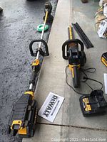 Overview showing string trimmer, hedge trimmer, charger, battery and manual on concrete surface