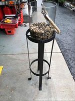 Front view of the black metal stand with cylindrical glass container filled with pebbles, showing stand's construction and height.
