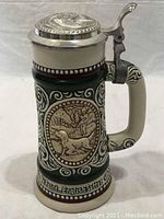 Front view showing hunting scene with hunter and dog, decorative scrollwork, and pewter lid with thumb lift.