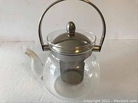 Front angle view showing glass body, metal lid, and handle with infuser inside.