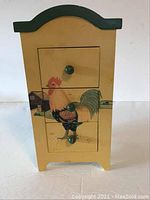 Front view of wooden three drawer box with hand painted rooster and green trim and knobs.