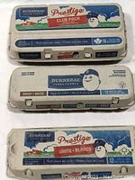 Photo of three empty Burnbrae Prestige egg cartons used for golf ball storage, showing brand and text.