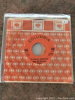 Single 45 RPM vinyl record visible in Columbia branded orange and white paper sleeve with label 'The Dangling Conversation' by Simon and Garfunkel