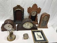 Photo showing all seven vintage clocks and framed design set on white cloth backdrop.