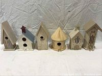 Photo showing all six decorative houses including four bird houses and two butterfly houses arranged in a row on a white surface against a white background
