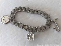 Sterling silver charm bracelet with three charms, laid flat to show the chain and charms distinctly.