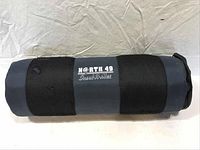 Rolled-up black and grey North 49 Insul-A-Mat sleeping pad for camping.