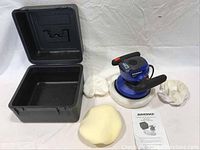 Overview of kit components including open black carrying case, Simoniz polisher, two white polishing bonnets, one yellow foam bonnet, and owner's manual on white backdrop.