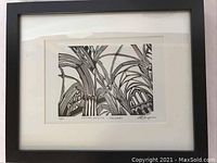 Full view of framed black and white numbered print under glass with black frame and white matting.