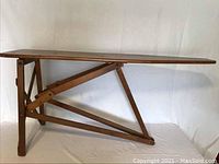 Full side view of the antique wooden ironing board showing the flat top and folding wooden stand.