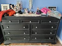 Black wooden long dresser with nine drawers and round handles, with various items placed on top.