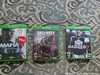 Photo showing three Xbox One game cases: Mafia III, Call of Duty Advanced Warfare Day Zero Edition, and Madden NFL 18.
